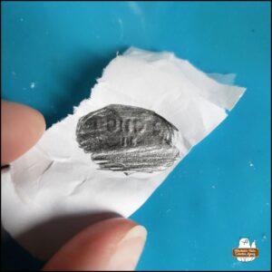 Fingers holding the paper that was the one used in pencil rubbing over the embossed characters from the bottom of the milk glass jar.