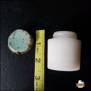 cleaned (side view) Pond's "artifact" jar and top of the light green (corroded) lid next to tape measure showing jar is approximately 2.25 inches and lid is 1.5 inches