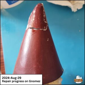 close up of the right side of the tip of the gnome's conical hat during repairs showing cracks, super glue, and missing paint.