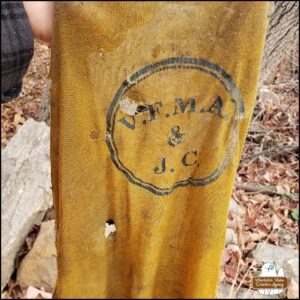 a piece of yellow fabric with lettering: V.F.M.A & J.C. inside a circle. The fabric is filthy and has holes. It was buried between rocks that had been excavated and moved. It looks more like it could have been a laundry bag rather than a shirt.