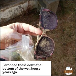 Amber's hand holding her old sunglasses which are covered in filth. caption: I dropped these down the bottom of the well house years ago.