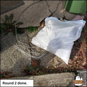 steel wire next to a white kitchen garbage bag full of litter collected from the embankment of the road. caption: Round 2 done.