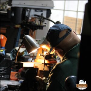 Over the left shoulder of the Grumpy Old Man at a workbench sharpening a chainsaw chain.